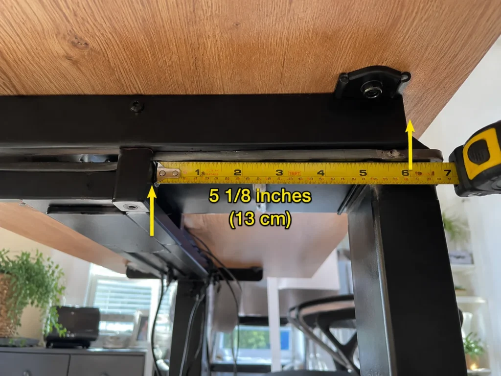 Measuring tape showing 5 1/8 inches of clearance between a standing desk crossbar and the desktop edge